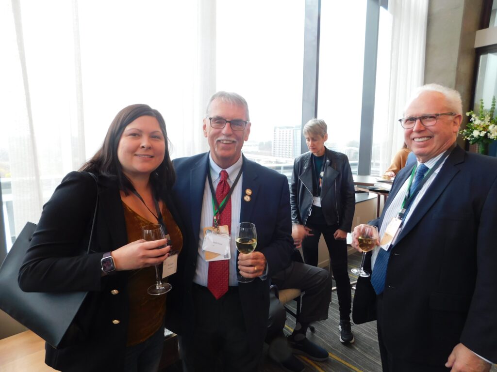two men and a woman standing next to each other holding wine glasses