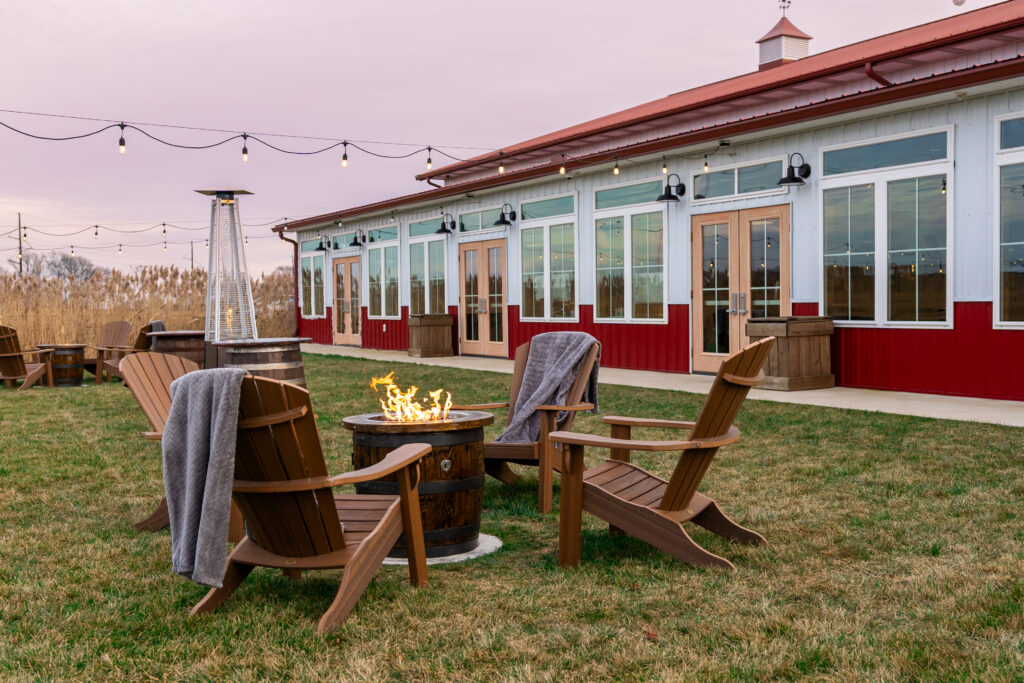 A lit firepit surrounded by Adirondack chairs in the back yard of the pole barn at King Cole Farm.
