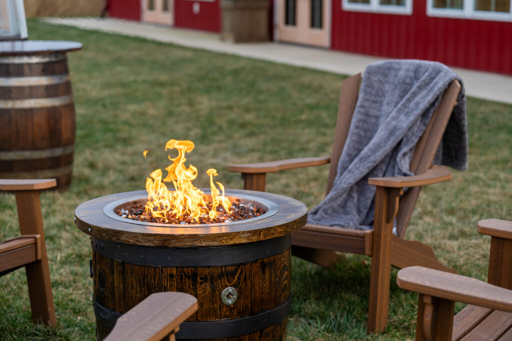 A lit firepit surrounded by Adirondack chairs in the back yard of the pole barn at King Cole Farm.