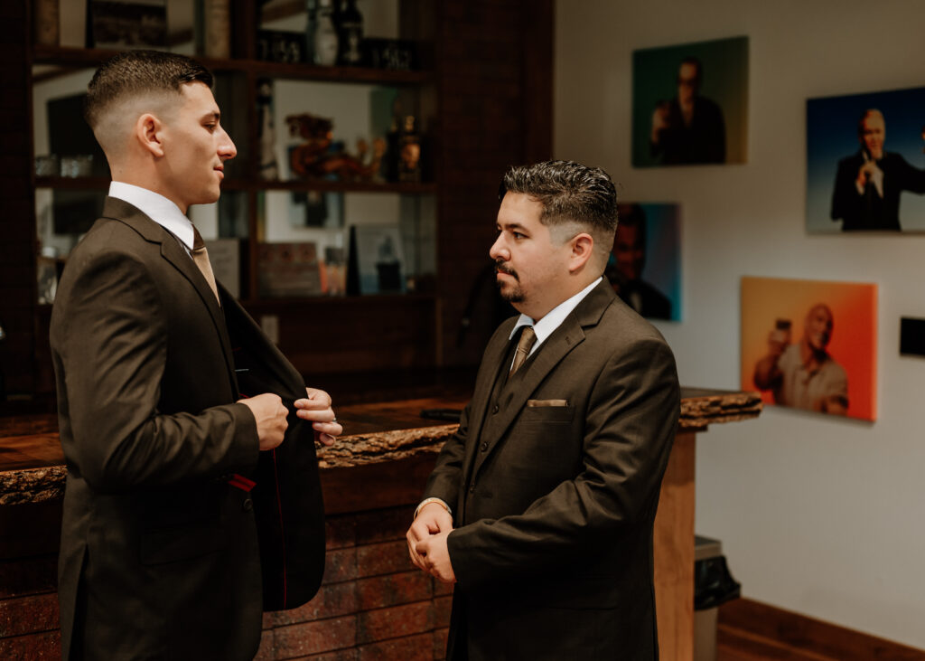 A groom and his groomsmen putting on suit jackets in the groomsmen's lodge in the pole barn at king cole farm.