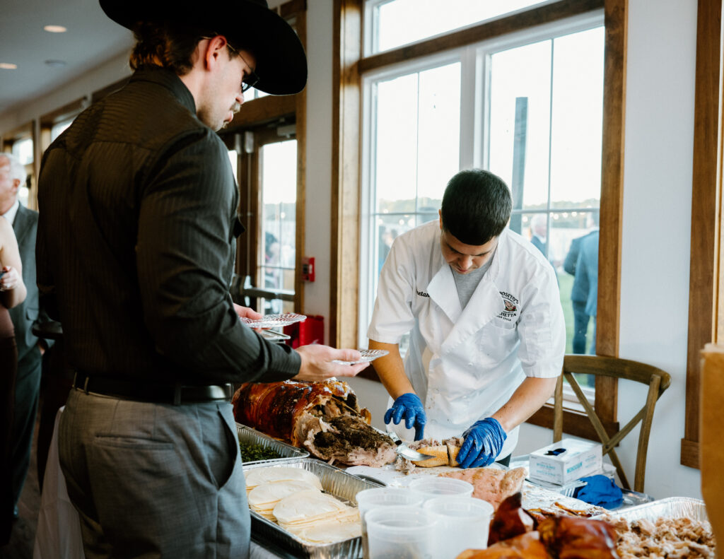 A caterer carving a roasted pig for guests during cocktail hour in the sunporch at King Cole Farm.