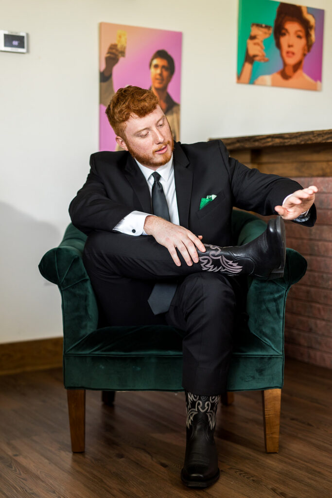 A groom sitting in a chair dusting off his shoe in the groom's lodge in the Pole Barn at King Cole Farm.