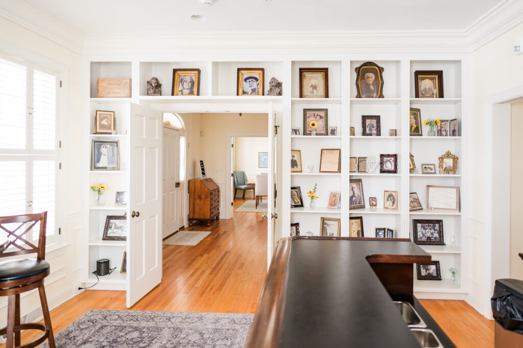 Image including the decorative shelves featuring wall art and trinkets, and a high top table with chairs in the Prohibition Bar in The Residence at King Cole Farm.