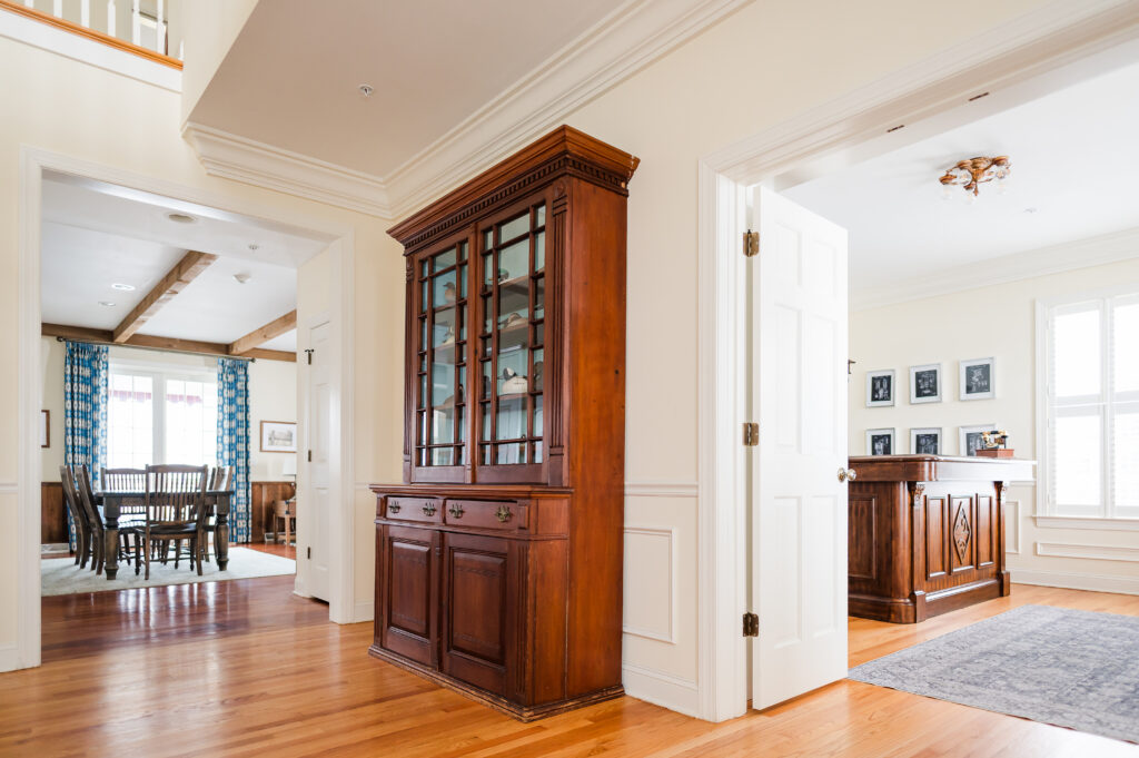 Image including the hallway just outside of the prohibition bar. The prohibition bar features a bar, wall art, instruments, old record player, and a high top table with chairs in the Prohibition Bar in The Residence at King Cole Farm.
