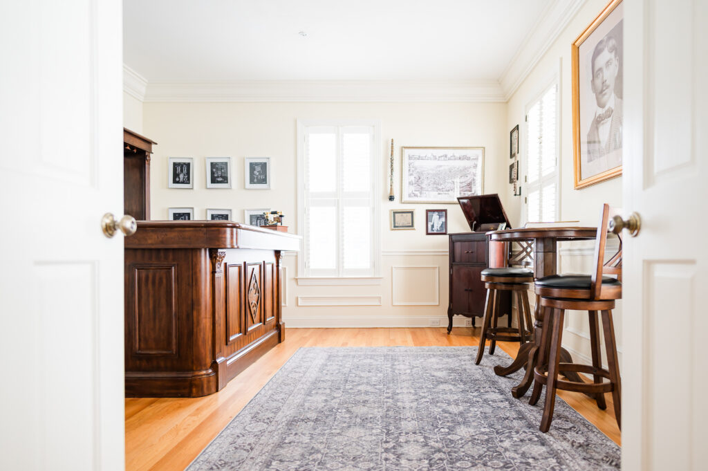 Image including the entrance of the prohibition bar featuring a bar, wall art, instruments, old record player, and a high top table with chairs in the Prohibition Bar in The Residence at King Cole Farm.
