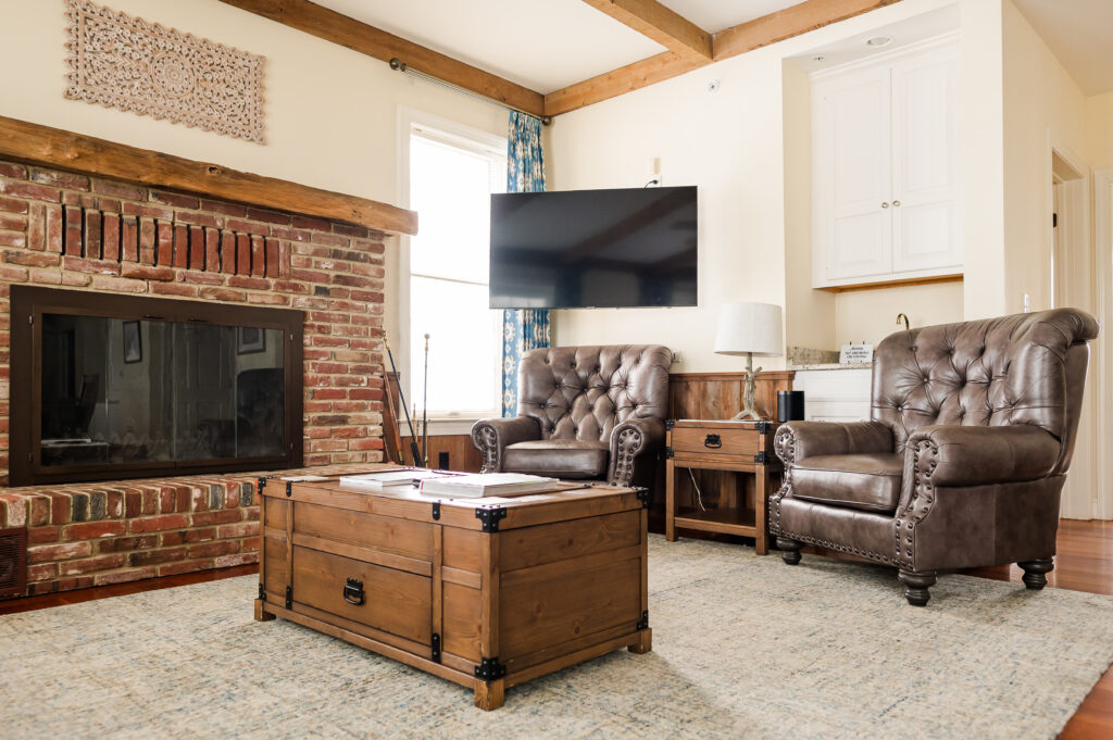 Image including a coffee table, fire place, side table, chairs, tv, and curtains in The Residence at King Cole Farm.