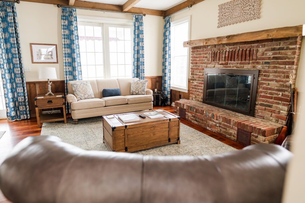Image including a couch, coffee table, fire place, side table, and curtains in The Residence at King Cole Farm.