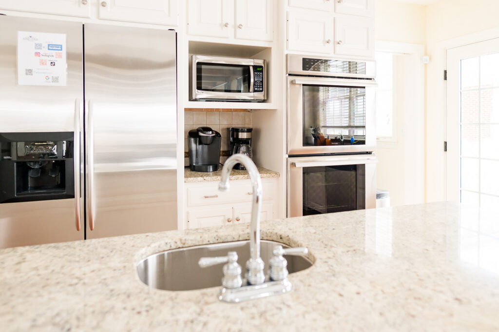 Image including the kitchen countertops, kitchen island with sink, refrigerator, keurig, coffee pot, and double ovens in the Residence at King Cole Farm.