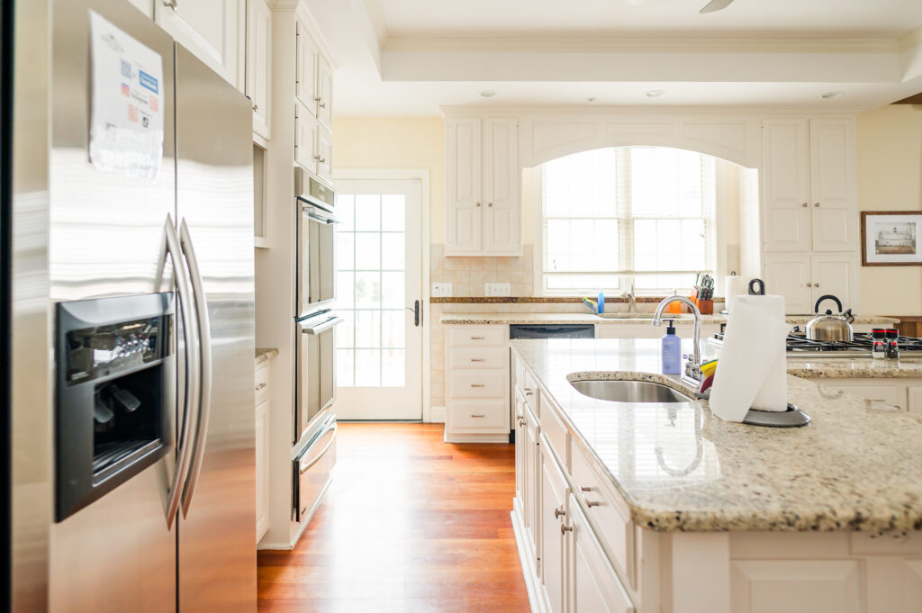Image including the kitchen countertops, kitchen island with sink, refrigerator and freezer, double oven, and windows and door to back patio in the Residence at King Cole Farm.3