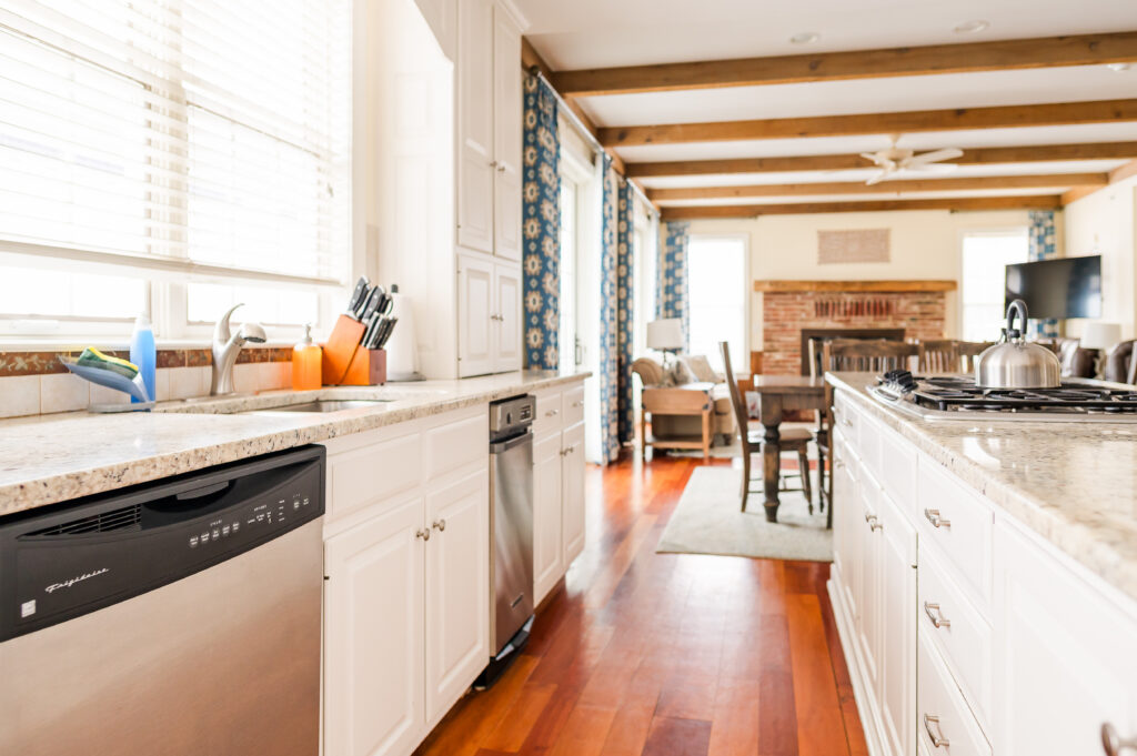 Image including the kitchen countertops, kitchen island with range, wall art, kitchen table, fireplace, tv, and overlooking the living room in the Residence at King Cole Farm.
