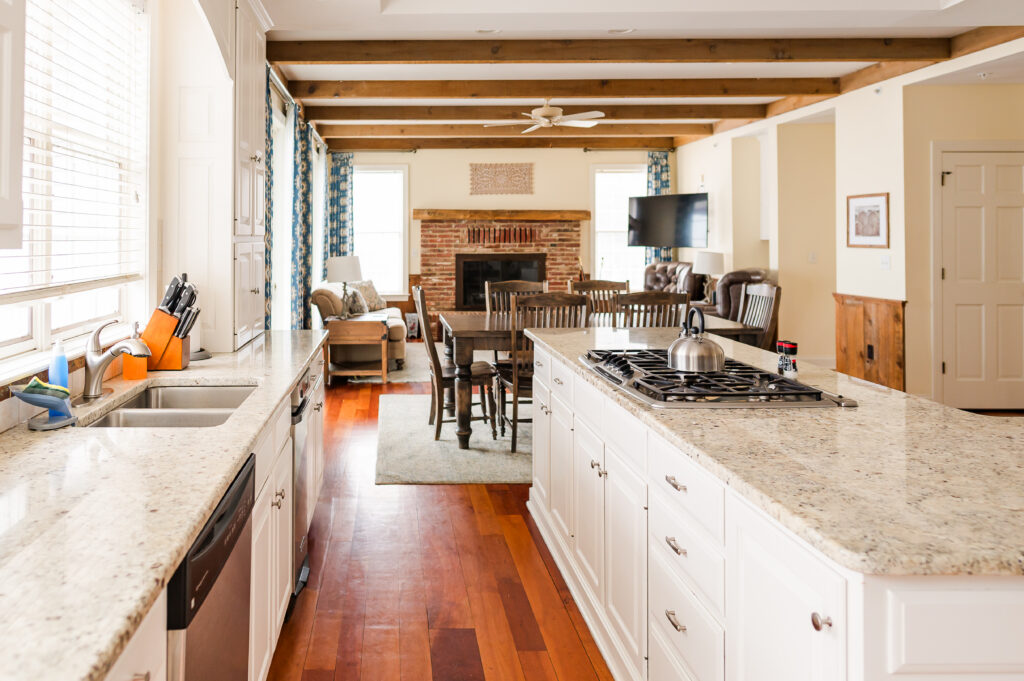 Image including the kitchen countertops, kitchen island with range, wall art, kitchen table, fireplace, tv, and overlooking the living room in the Residence at King Cole Farm.