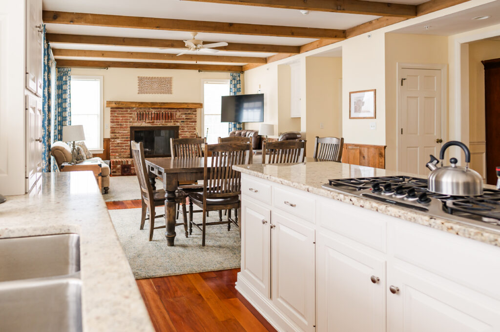 Image including the kitchen countertops, kitchen island with range, wall art, kitchen table, fireplace, tv, and overlooking the living room in the Residence at King Cole Farm.