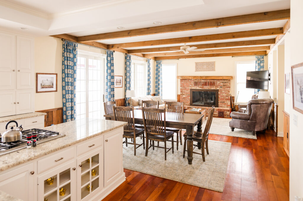 Image including the kitchen, dining table and chairs, and living room with fireplace, wall art, couch, and two chairs in the Residence at King Cole Farm.