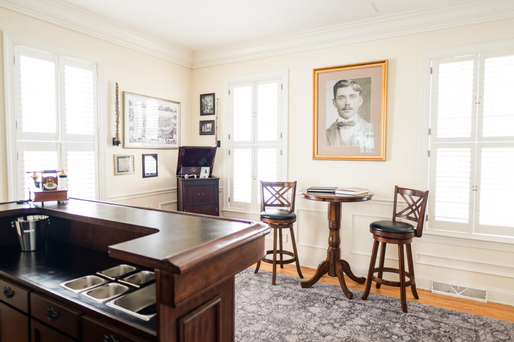 Image including a bar, wall art, instruments, old record player, and a high top table with chairs in the Prohibition Bar in The Residence at King Cole Farm.