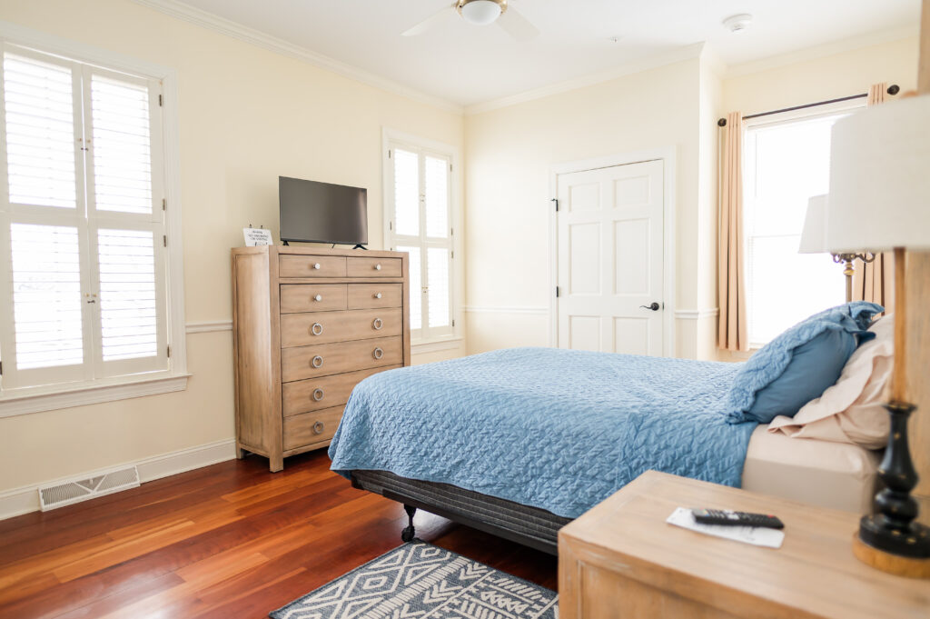 Image featuring queen size bed, side table, dresser with tv, closet, and windows in the ADA Bedroom at The Retreat at King Cole Farm.