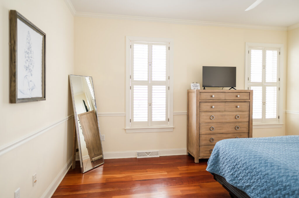 Image featuring queen size bed, floor mirror, dresser with tv, wall art, and windows in the ADA Bedroom at The Retreat at King Cole Farm.