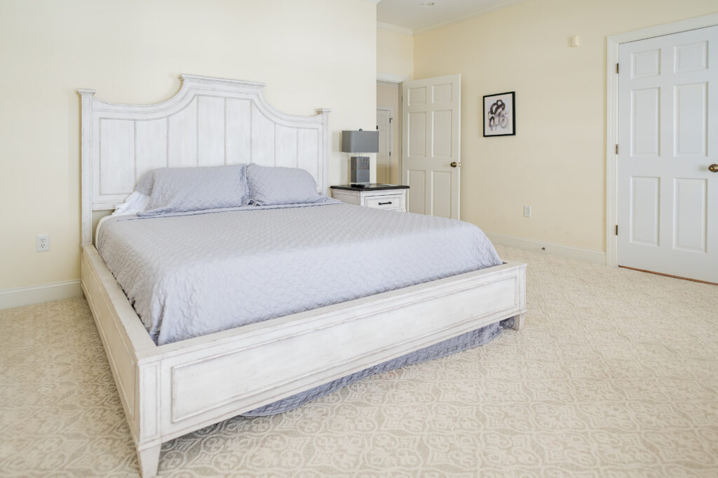 Image featuring the king bed, side table, room entrance, art, and closets in the Sunset Bedroom in the Retreat at King Cole Farm.