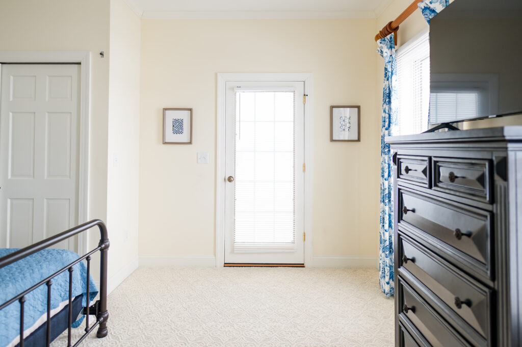 Image of a bed, dresser with TV, closet, and door leading out to the shared balcony in the Bayview Room at King Cole Farm.