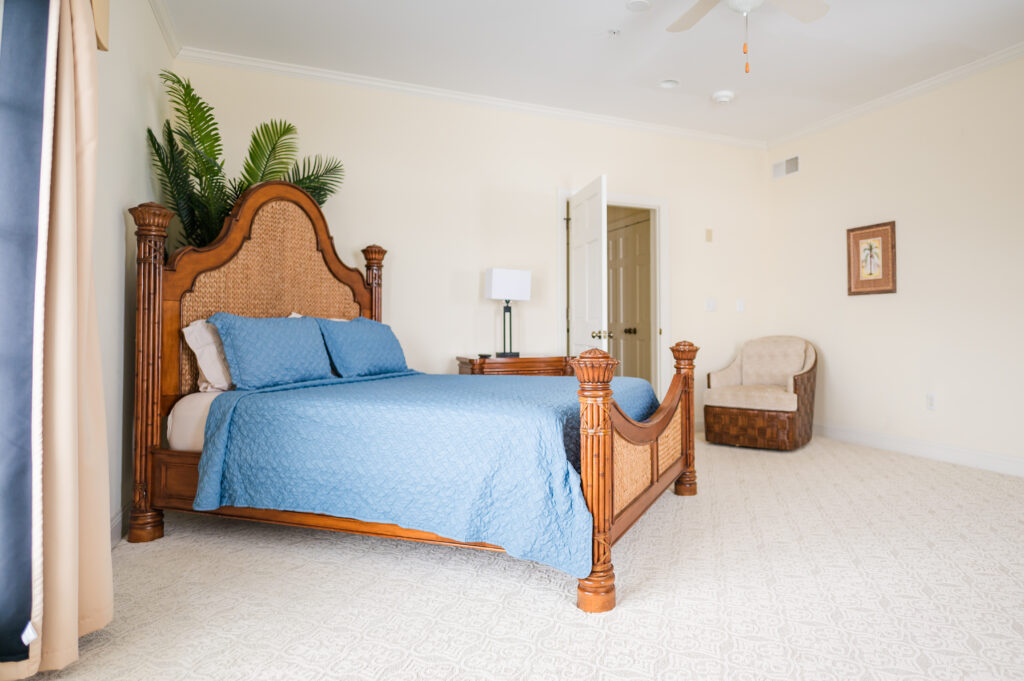 Image featuring a bed, swivel chair, nightstand with a lamp, and decorative palm tree in the Island Sun Bedroom at King Cole Farm