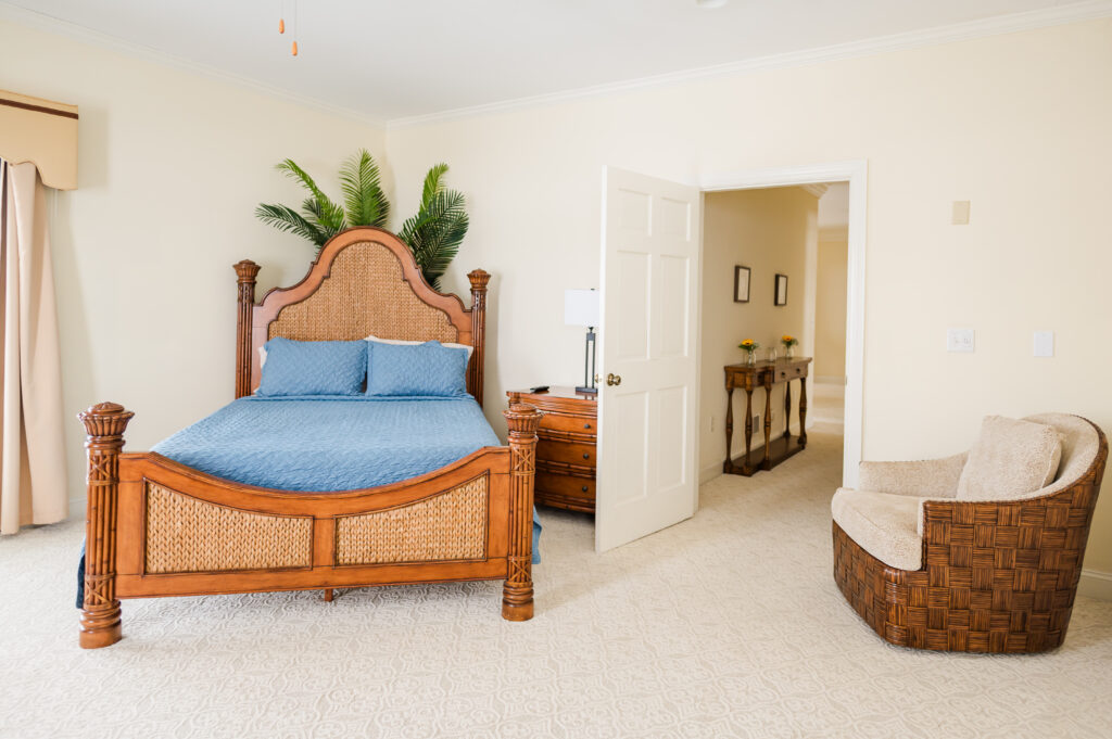 Image featuring a bed, swivel chair, nightstand with a lamp, doorway, and decorative palm tree in the Island Sun Bedroom at King Cole Farm