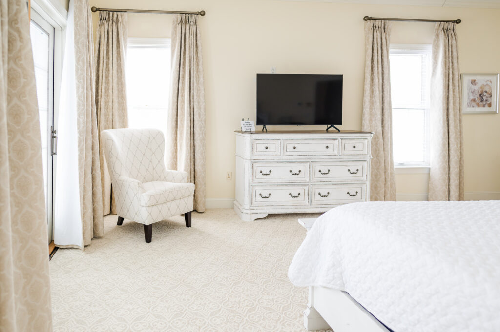 Image of the dresser, tv, chair, bed, and windows with draping in the bridal suite bedroom at King Cole Farm