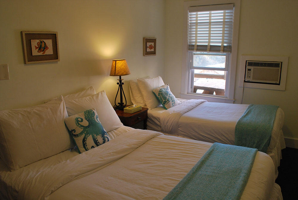 two beds in a bedroom with white sheets and blue pillows
