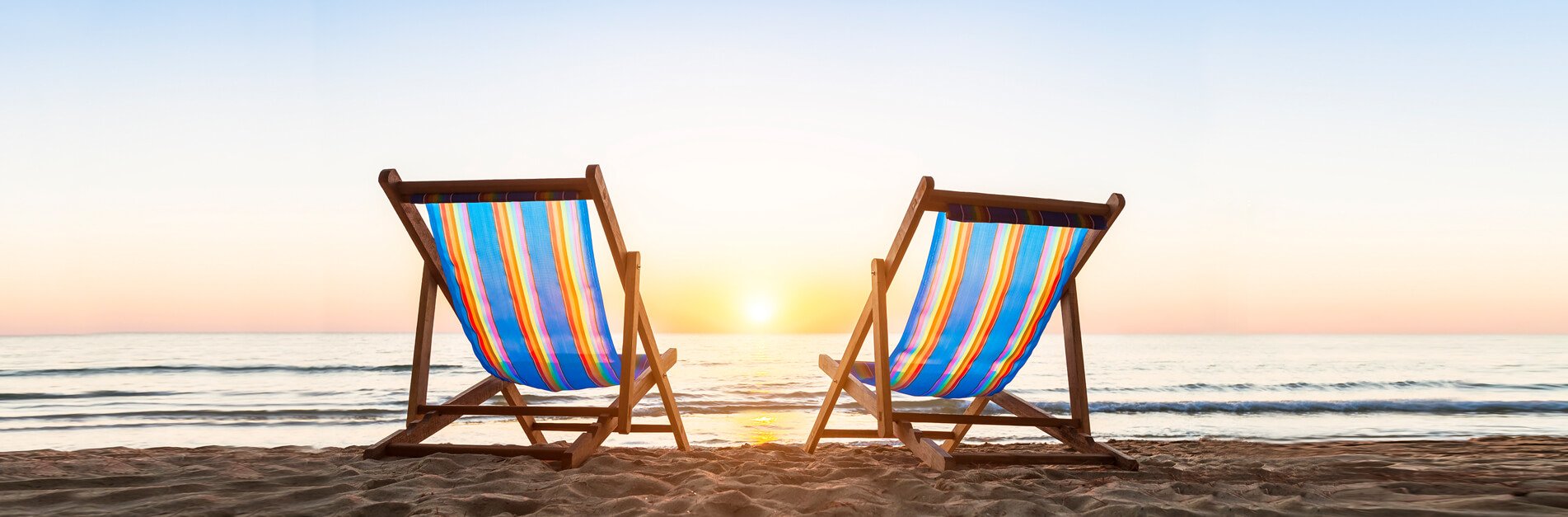 Two beach chairs facing the ocean at sunset.