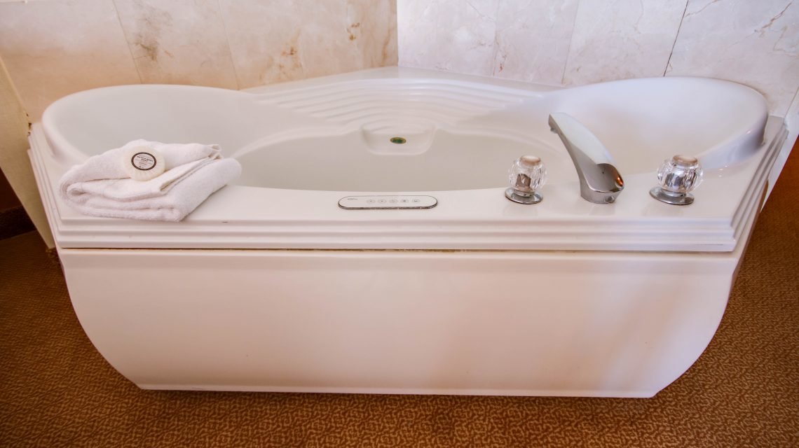 A large white jacuzzi tub with silver fixtures and a stack of white towels on the left side