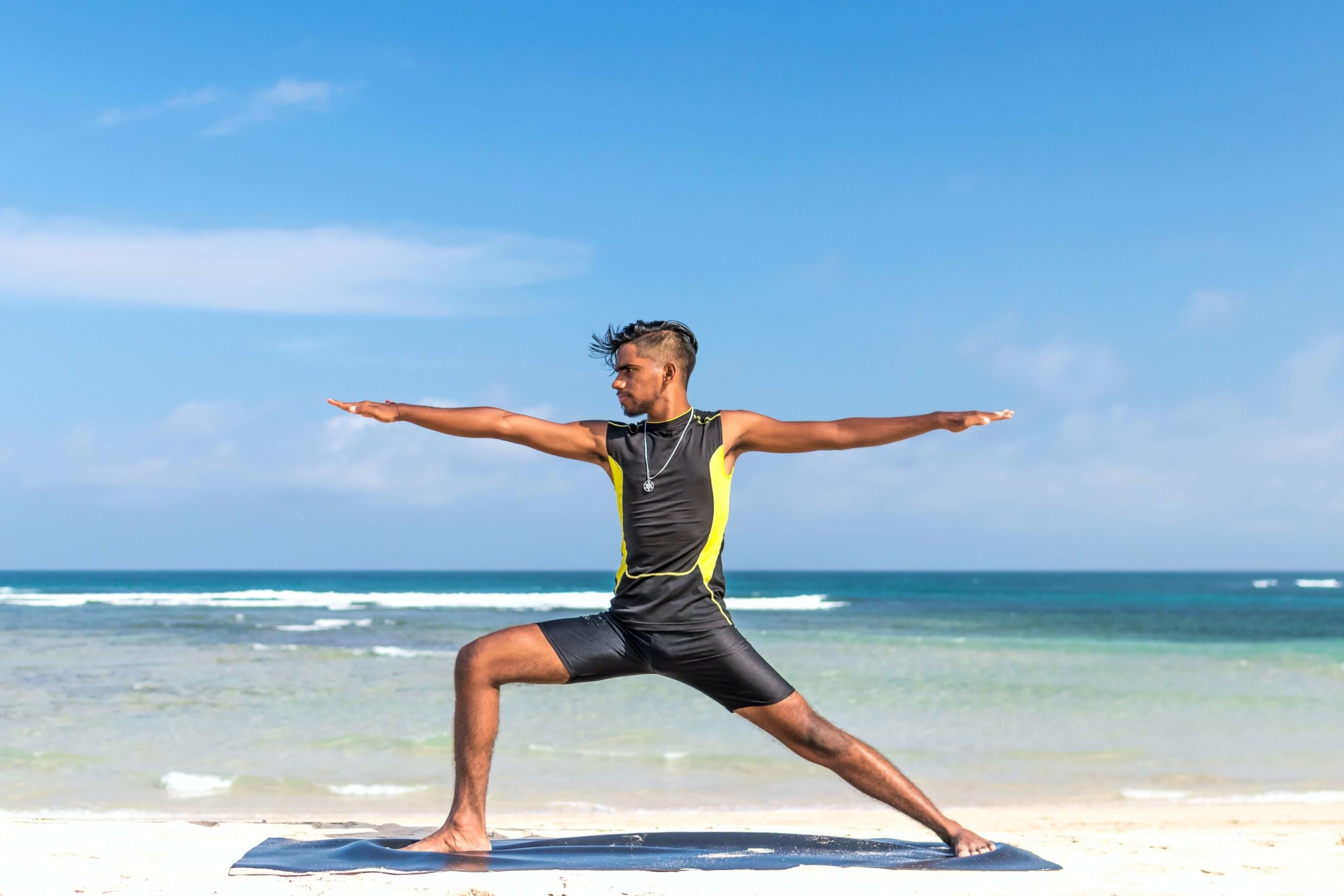 male on beach doing yoga with ocean behind him