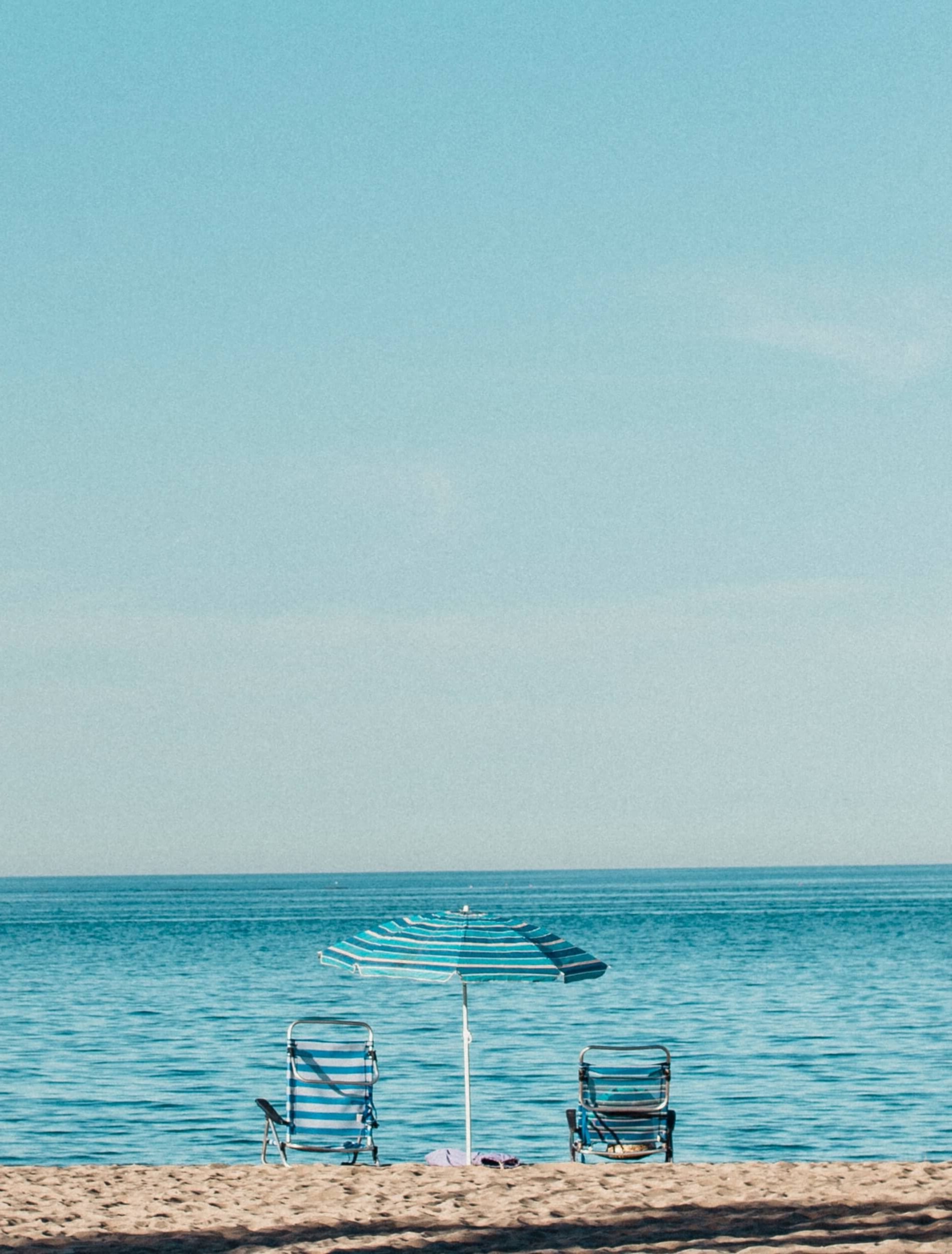 a beach with two chairs and an umbrella