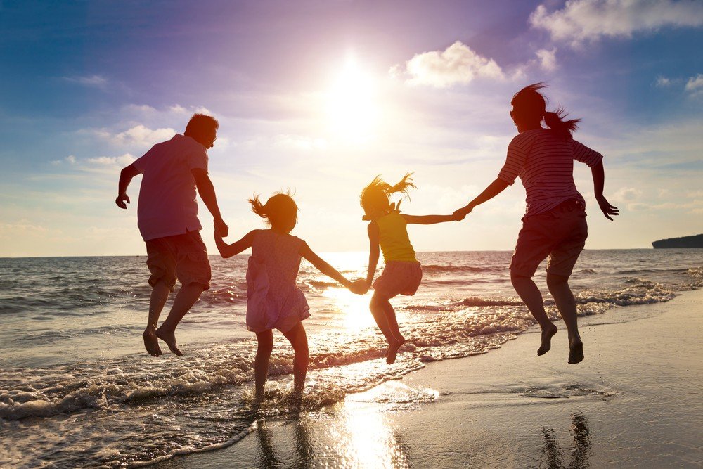 family of four playing on beach jumping waves