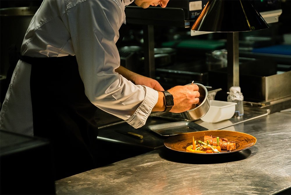 chef pouring sauce on dish in kitchen