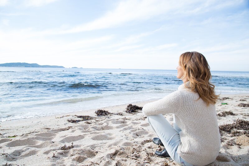 female sitting on beach facing ocean