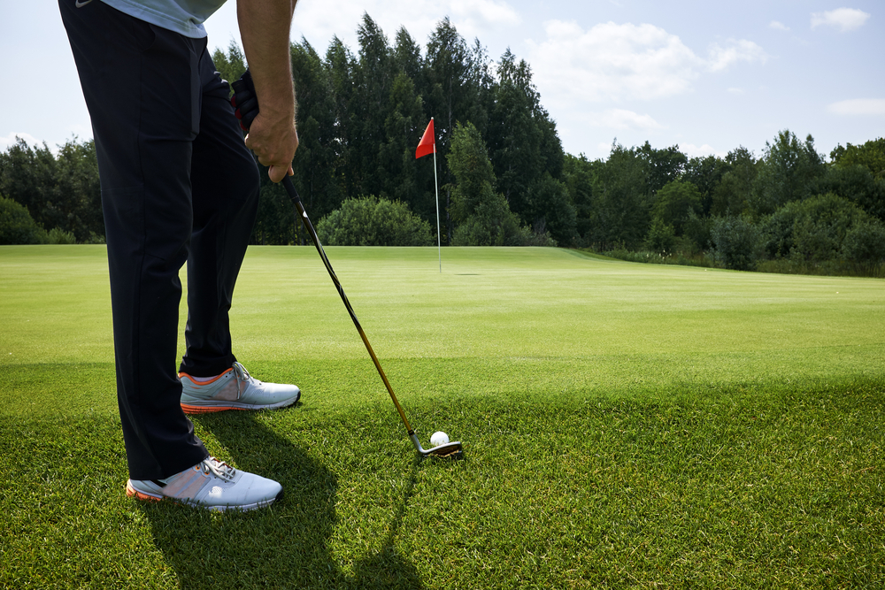 close up of golfer holding golf club by green