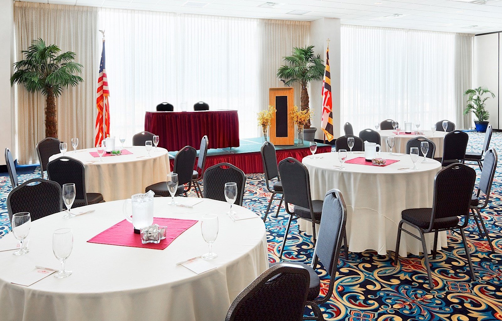 A meeting room with round tables, black chairs, and a stage in the background.