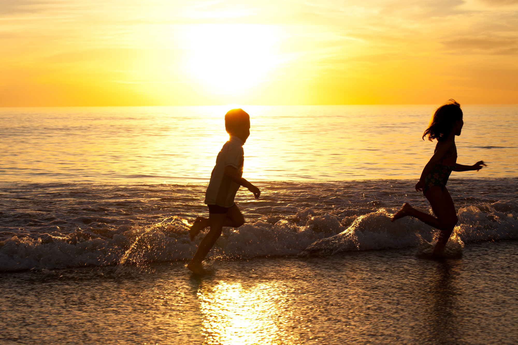 Two children running in the ocean at sunset.