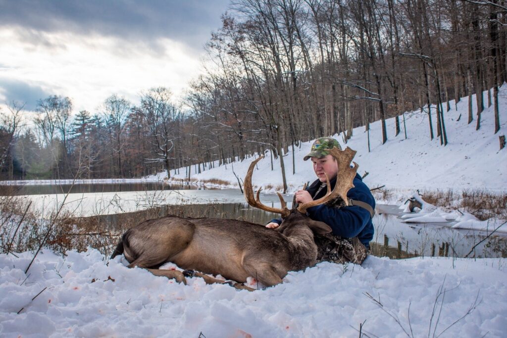 a woman sitting next to a deer in the snow