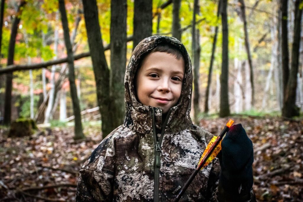 a young boy in a camouflage jacket holding an umbrella