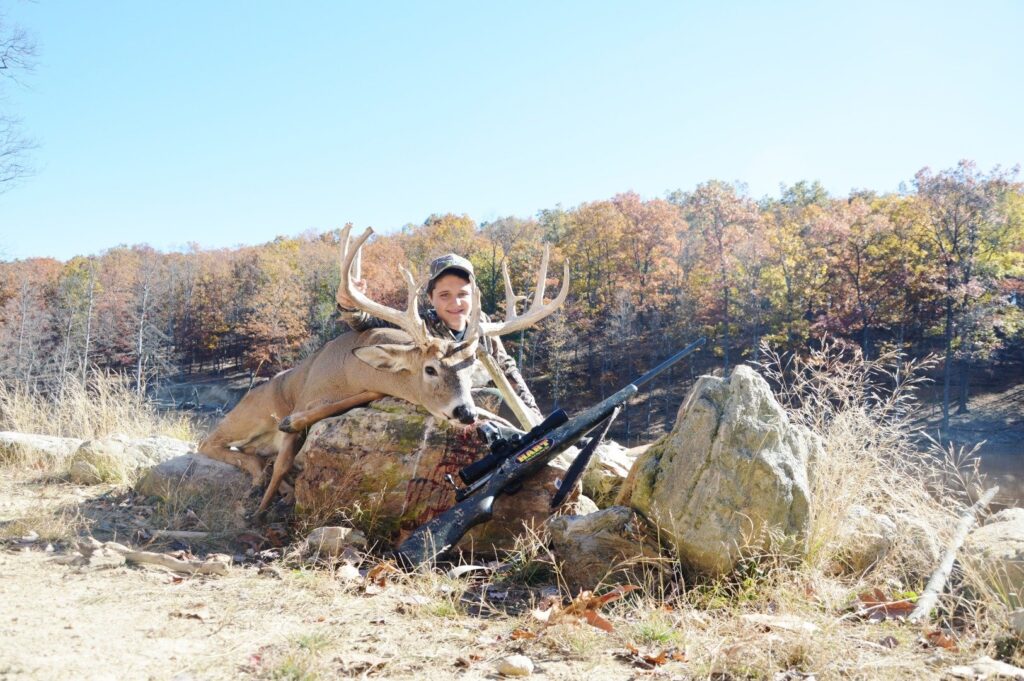 a man kneeling down next to a deer with a rifle