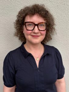 a woman wearing glasses standing in front of a wall