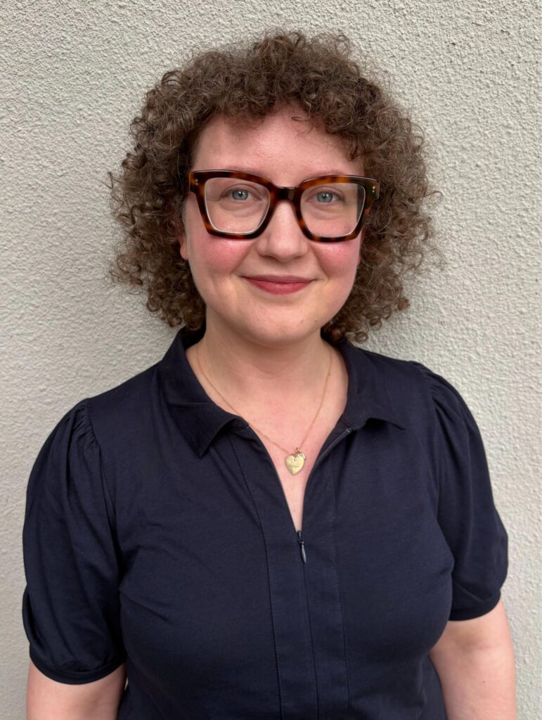 a woman wearing glasses standing in front of a wall