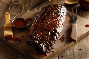 Ribs on a cutting board with sauce and knife.