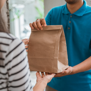 One person handing another a brown paper bag of food