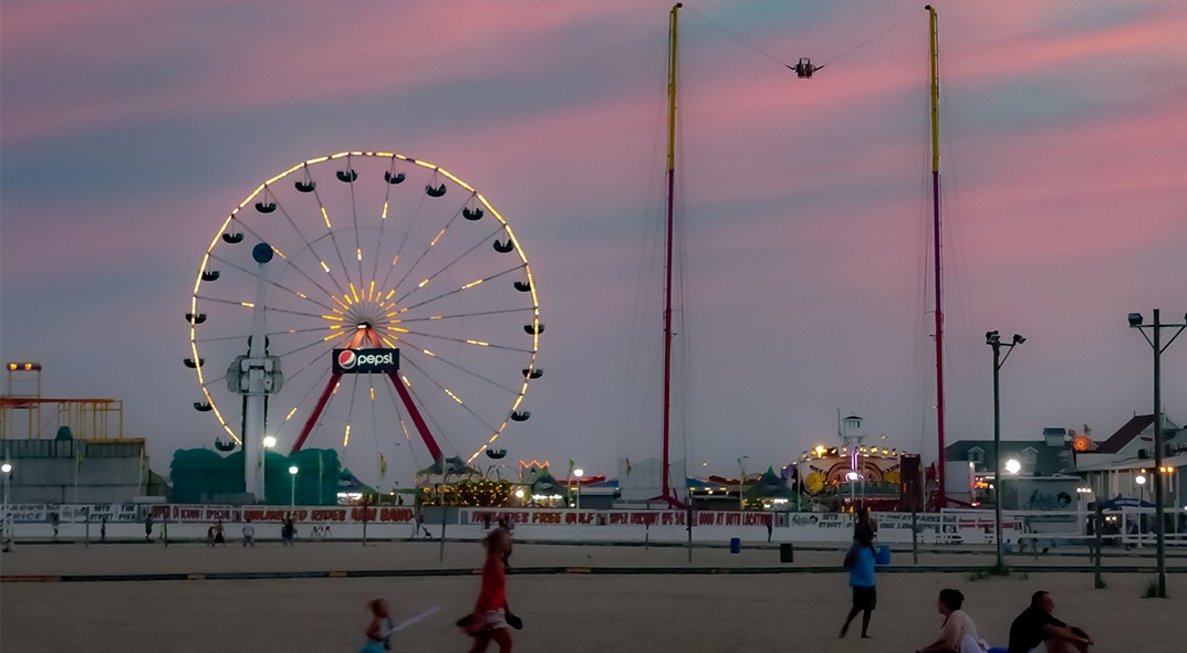 a beach scene at sunset with a large Ferris wheel in the background
