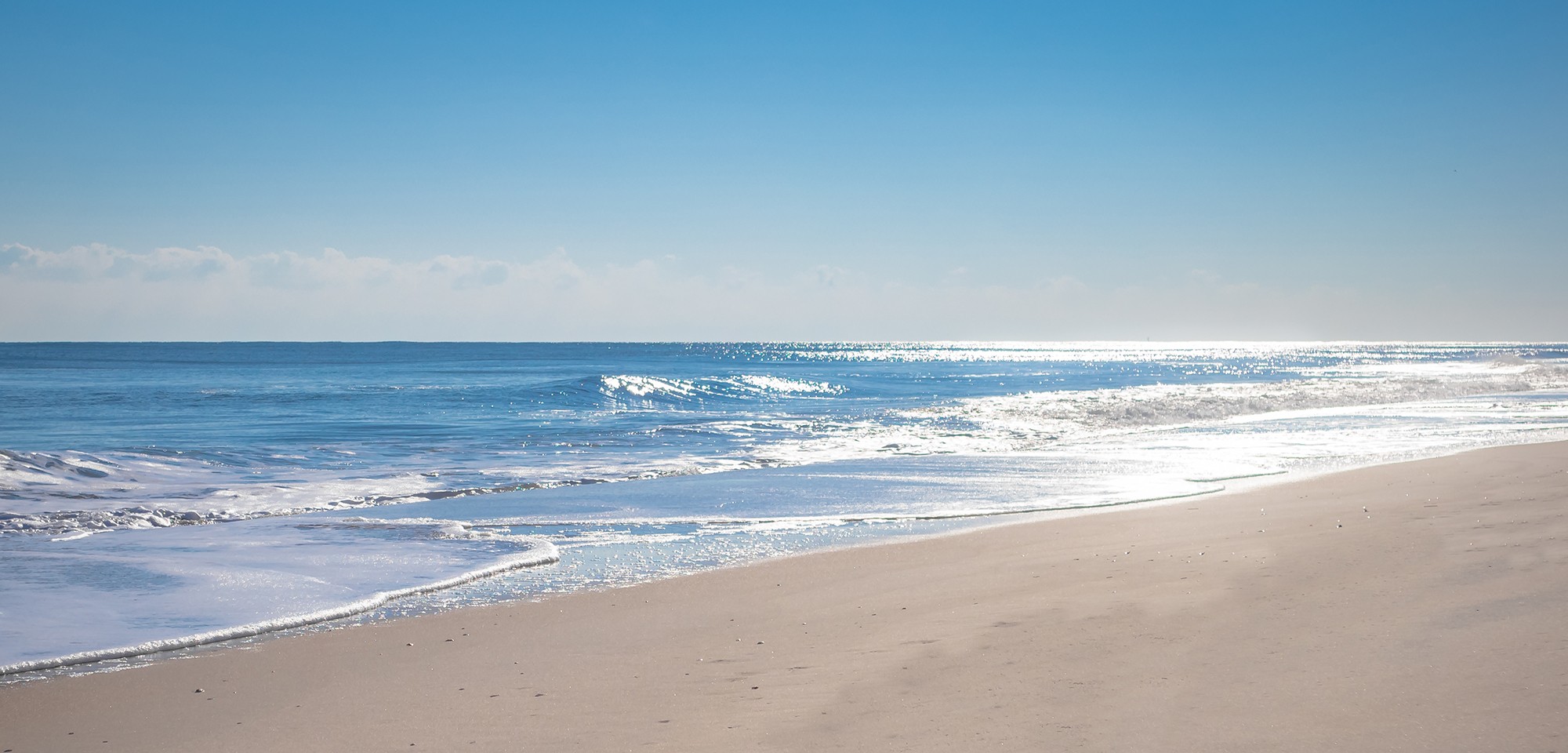 A serene beach scene with waves gently lapping at the shore under a clear blue sky.