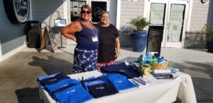 two women standing in front of a table with shirts on it