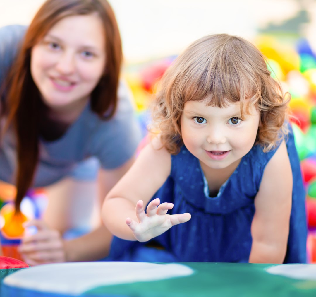 Happy little girl having fun in colourful plastic balls pool with her mother