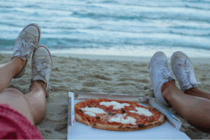 two people sitting on a beach with a pizza