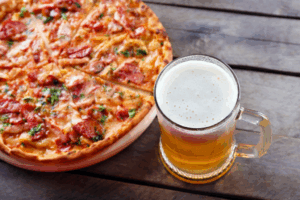 a pizza sitting on top of a wooden table next to a glass of beer