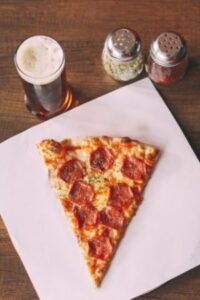 a slice of pizza on a napkin next to a pint of beer